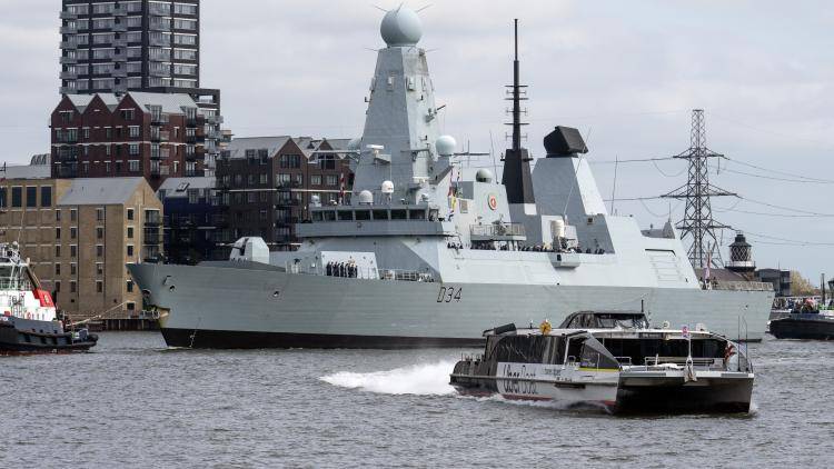 A Royal Navy destroyer underway in harbour with a ferry in the foreground